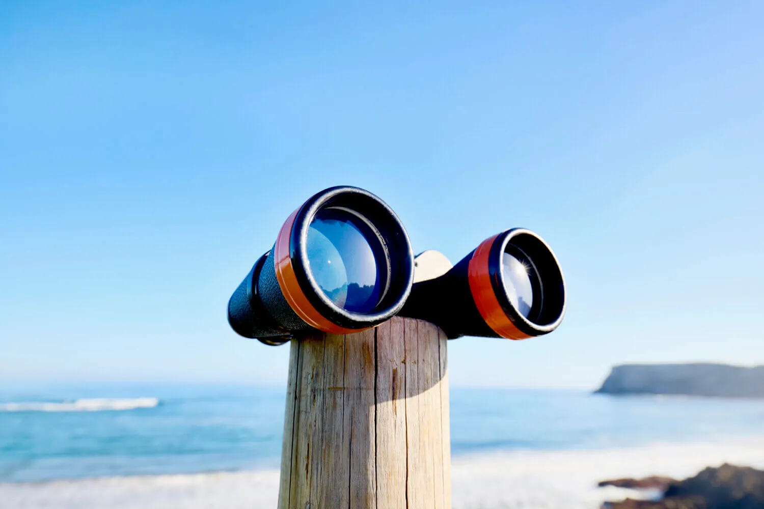 Binoculars on wooden pole by the sea against blue sky